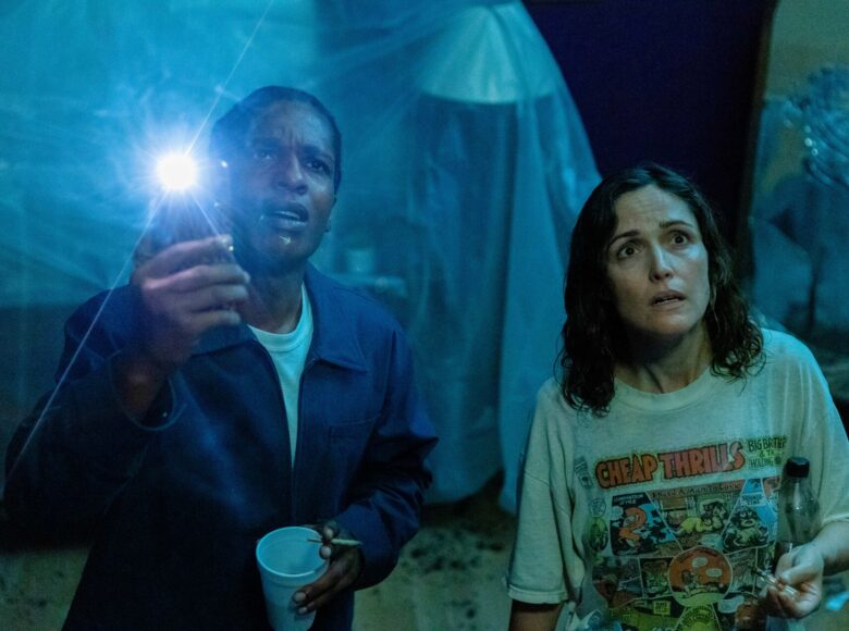 Fotos z filmu. Na pierwszym planie stoją obok siebie biała kobieta i czarny mężczyzna. Patrzą do góry z zaniepokojonymi twarzami. Za nimi pogrążone w półmroku pomieszczenie.
