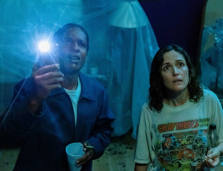 Fotos z filmu. Na pierwszym planie stoją obok siebie biała kobieta i czarny mężczyzna. Patrzą do góry z zaniepokojonymi twarzami. Za nimi pogrążone w półmroku pomieszczenie.