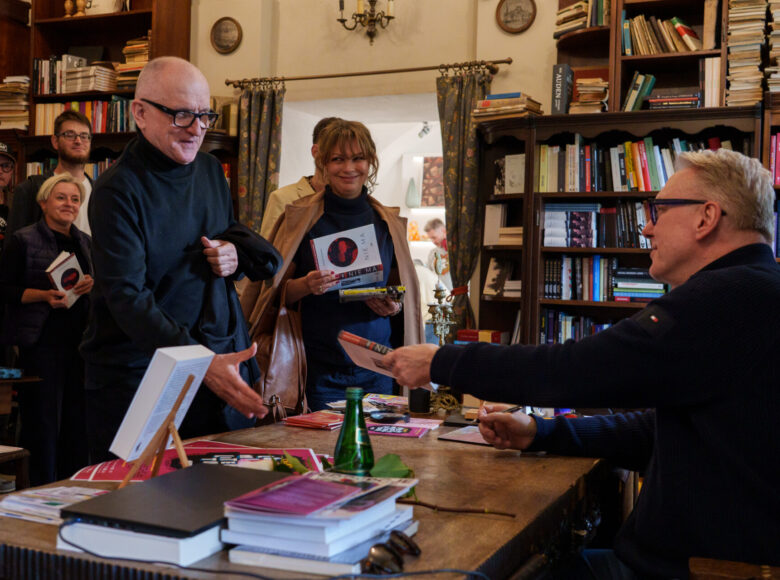Wnętrze Księgarni Dosłownej w Centrum Kultury w Lublinie. Przy biurku siedzi pisarz Mariusz Szczygieł, podpisujący swoje książki. Przed nim kolejka uśmiechających się osób z książkami do podpisania.