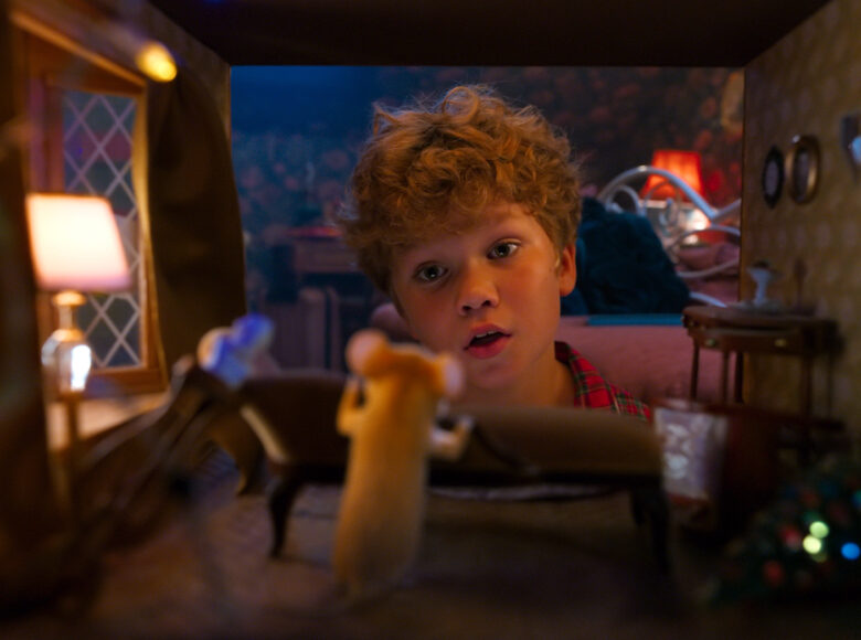 Zbliżenie na twarz chłopczyka zaglądającego do domku dla lalek. Chłopczyk patrzy na animowaną sylwetkę myszki, stojącą w domku.