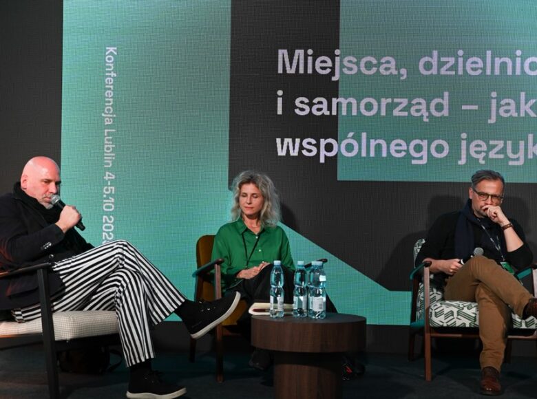 Fotografia z konferencji. Na scenie siedzą trzy osoby, kobieta i dwóch mężczyzn. Jeden z mężczyzn - dyrektor Centrum Kultury w Lublinie - trzyma w ręku mikrofon i mówi coś do niego.