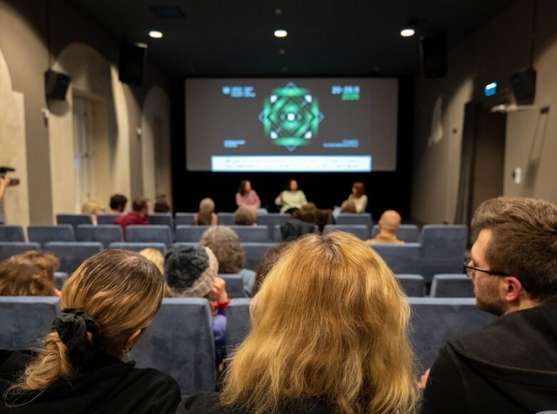 Sala Widowiskowa Centrum Kultury w Lublinie. Widok na scenę z perspektywy widowni. Na pierwszym planie osoby siedzące na widowni widziane od tyłu. W głębi trzy osoby siedzące na scenie, widziane od przodu. Za nimi wisi logo Lubelskiego Festiwalu Filmowego.