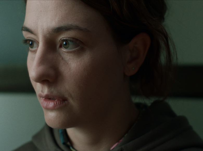 Zbliżenie na twarz młodej kobiety, patrzącej na coś poza kadrem.