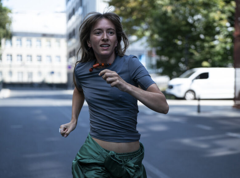 Lato, ciepły dzień. Zbliżenie na młodą kobietę biegnącą miejską ulicą.