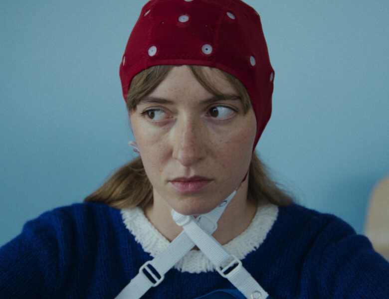 kadr z filmu. Zbliżenie na twarz młodej dziewczyny w czepku o nieokreślonej funkcji. Za nią widzimy fragment pulpitu, który może się kojarzyć z jakimś urządzeniem medycznym. W tle niebieska ściana.