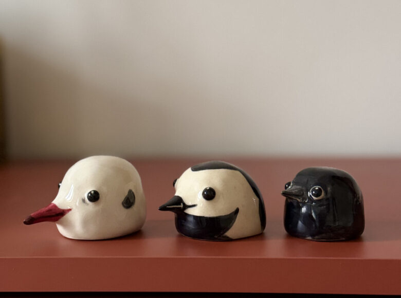 Na szafce stoją trzy kolorowe ceramiczne figurki, przedstawiające ptaszki.