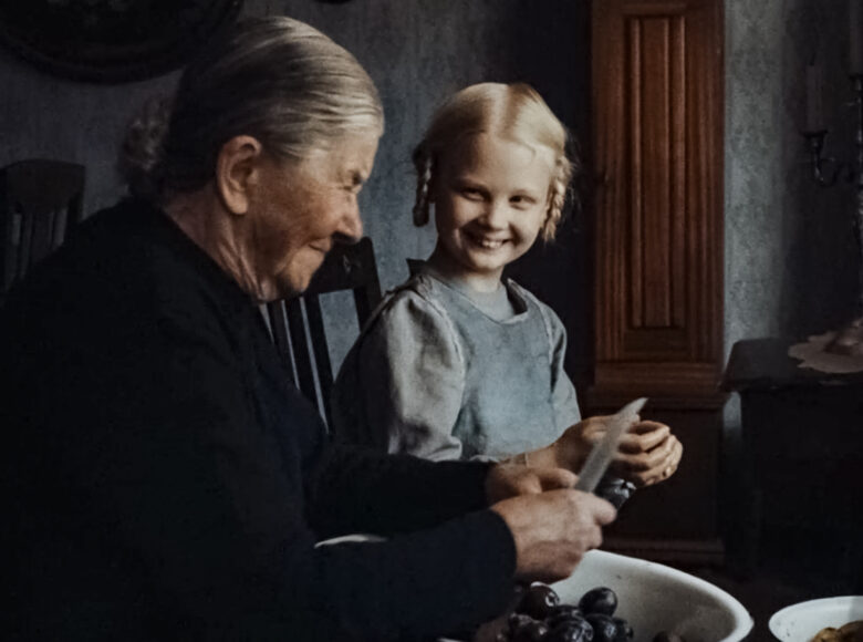 W staroświecko urządzonym pokoju siedzą przy stole stara kobieta i kilkuletnia dziewczynka, ubrane w dawne stroje. Uśmiechają się do siebie. Kobieta wykrawa nożem pestki ze śliwek, które stoją przed nią w misce.