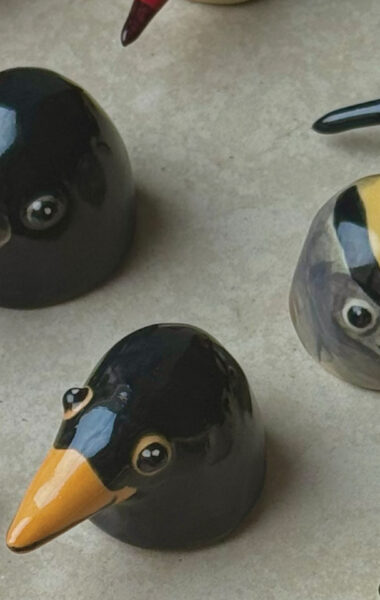 Na blacie stołu stoi kilka kolorowych, ceramicznych figurek. Przedstawiają one ptaszki.