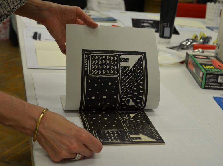 Zbliżenie na dłonie osoby zdejmującej z matrycy graficznej kawałek papieru ze świeżo wykonaną odbitką.