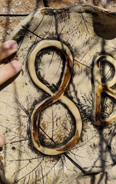 Zbliżenie na męską dłoń, dotykającą płaskorzeźby, która przytwierdzona jest do muru.