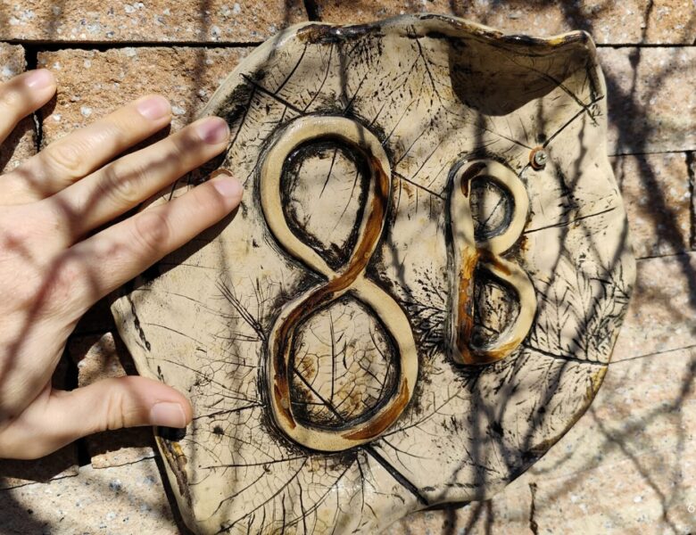 Zbliżenie na męską dłoń, dotykającą płaskorzeźby, która przytwierdzona jest do muru.