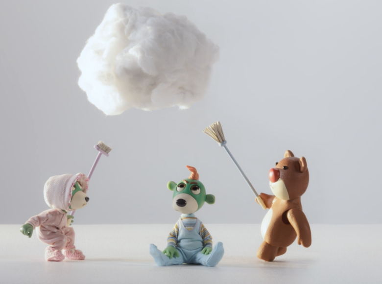 Kadr z filmu animowanego. Puste pomieszczenie z białą podłogą i białą ścianą. Na środku na podłodze siedzi miś. Po obu jego stronach stoją dwa inne misie, trzymające w rękach miotły skierowane do góry. Nad misiami unosi się biała chmurka.