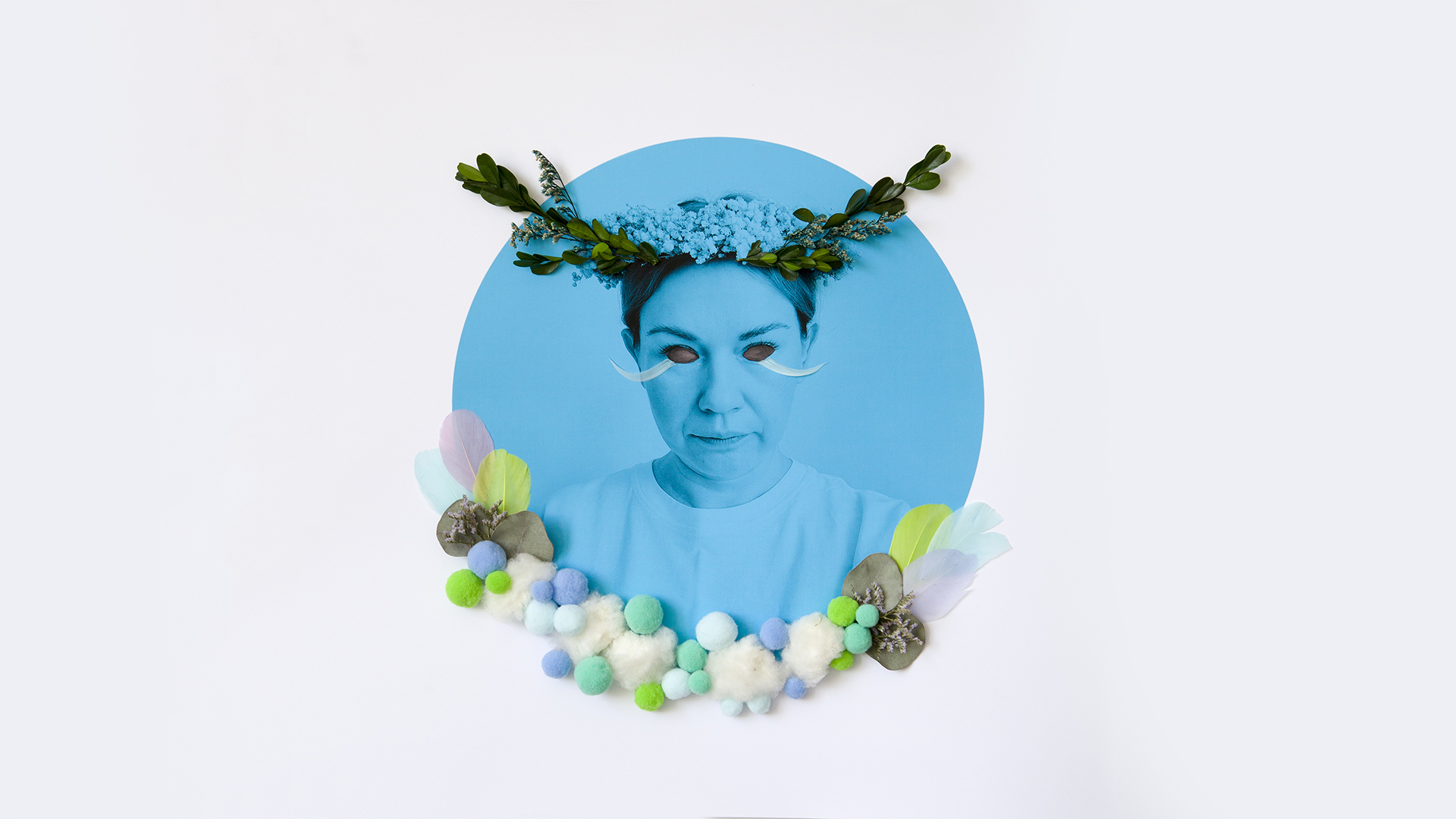 Kolorowa, surrealistyczna fotografia przedstawia pomalowaną na niebiesko twarz kobiety, umieszczoną w niebieskim okręgu na białym, prostokątnym tle. Jej oczy – również utrzymane w surrealistycznej estetyce – mają czerwony kolor. Kobieta ma na głowie upięte gładko włosy i wianek z biało-zielonych roślin. Jest ubrana w białą podkoszulkę. Kadr fotografii, na wysokości jej piersi zamyka półkolisty wianek wykonany z różnokolorowych małych kuleczek o różnej wielkości i kolorowych piór.
