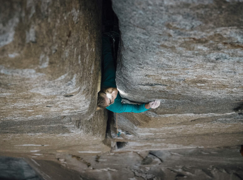 Pokazana od góry skała. W jej szczelinie widzimy osobę, która patrzy w górę, w obiektyw.