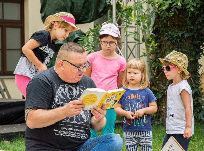 Wirydarz Centrum Kultury w Lublinie. Zbliżenie na aktora Dariusza Jeża, który czyta na głos książkę grupce otaczających go kilkuletnich dzieci.