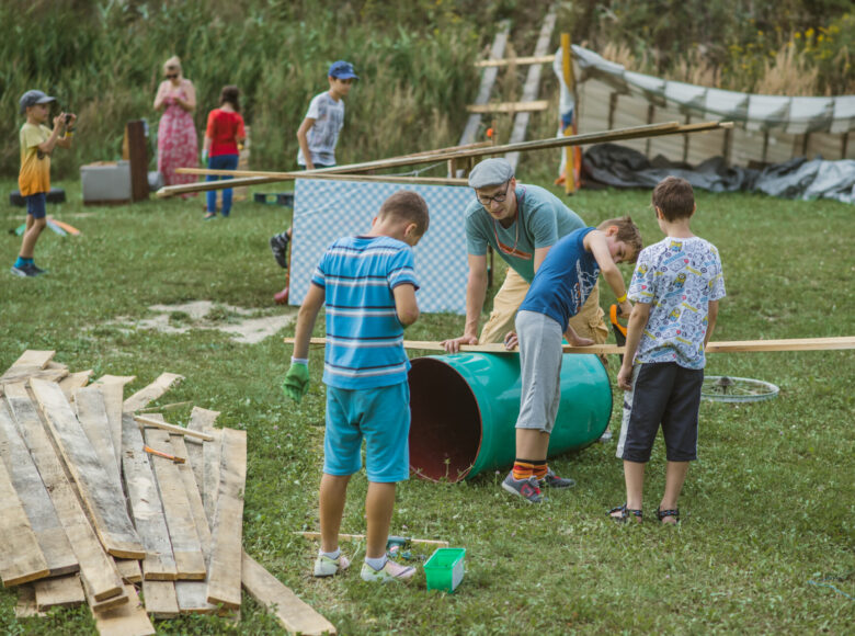 W plenerze, na trawie grupa dzieci bawi się i majsterkuje.
