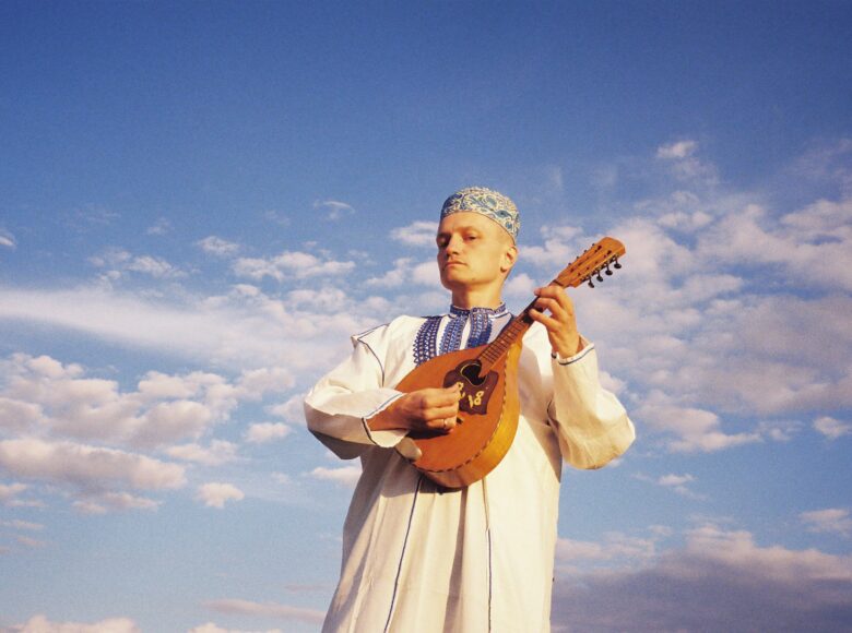 Na tle nieba stoi mężczyzna, grający na mandolinie.
