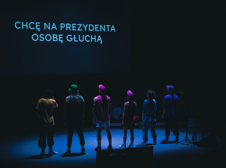 Przedstawienie teatralne. Na scenie grupa aktorów.