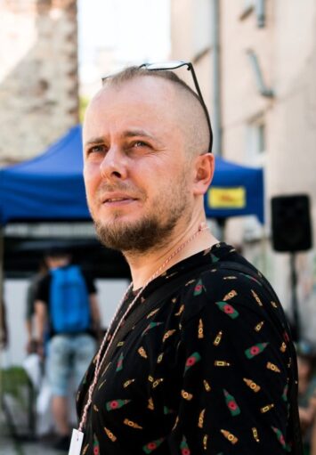 Zbliżenie na mężczyznę w średnim wieku, stojącego przed starą kamienicą miejską.