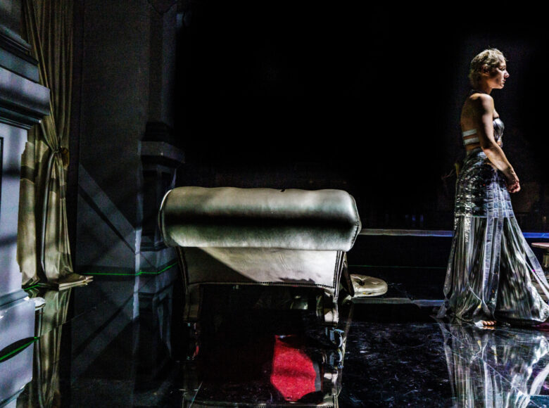 Przedstawienie teatralne. Na scenie stoi kobieta twarzą do widowni.