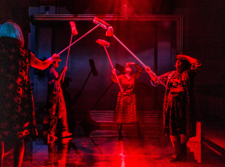 Przedstawienie teatralne. Na scenie cztery kobiety. Każda trzyma w ręku miotłę i podnosi ją do góry.