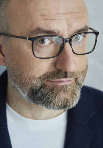 Fotograficzny portret mężczyzny w średnim wieku. Mężczyzna ma pociągłą twarz, ma krótką brodę i wąsy. Nosi okulary.