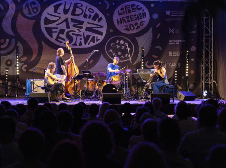 Nocny koncert na wirydarzu Centrum Kultury w Lublinie. Na pierwszym planie widzimy od tyłu widownię. Na drugim planie scenę z muzykami.