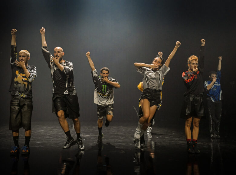 Spektakl teatru tańca. Na scenie grupa osób w dynamicznym układzie tanecznym.