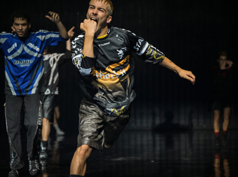 Spektakl teatru tańca. Na scenie grupa osób w dynamicznym układzie tanecznym.