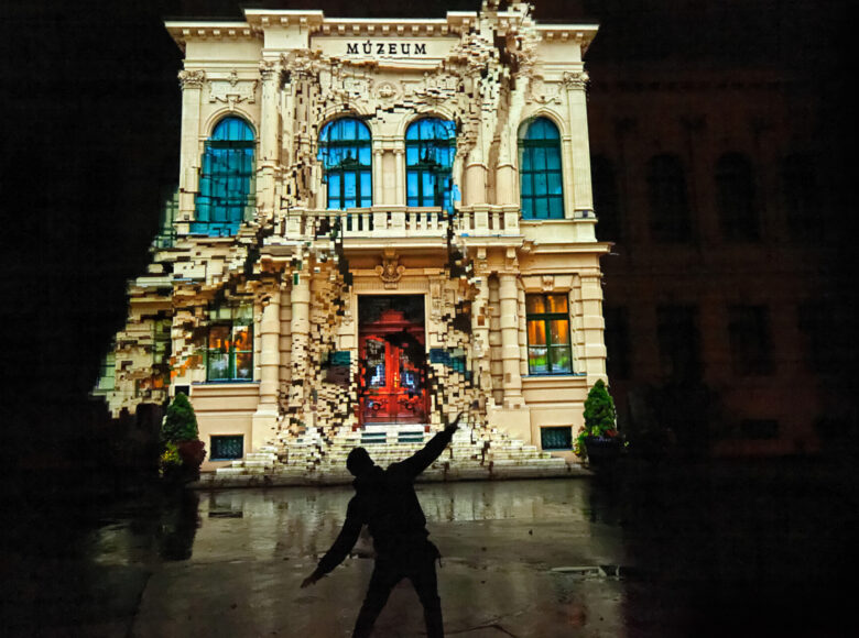 Na scenie tancerz tańca współczesnego na tle scenografii przedstawiającej architekturę.